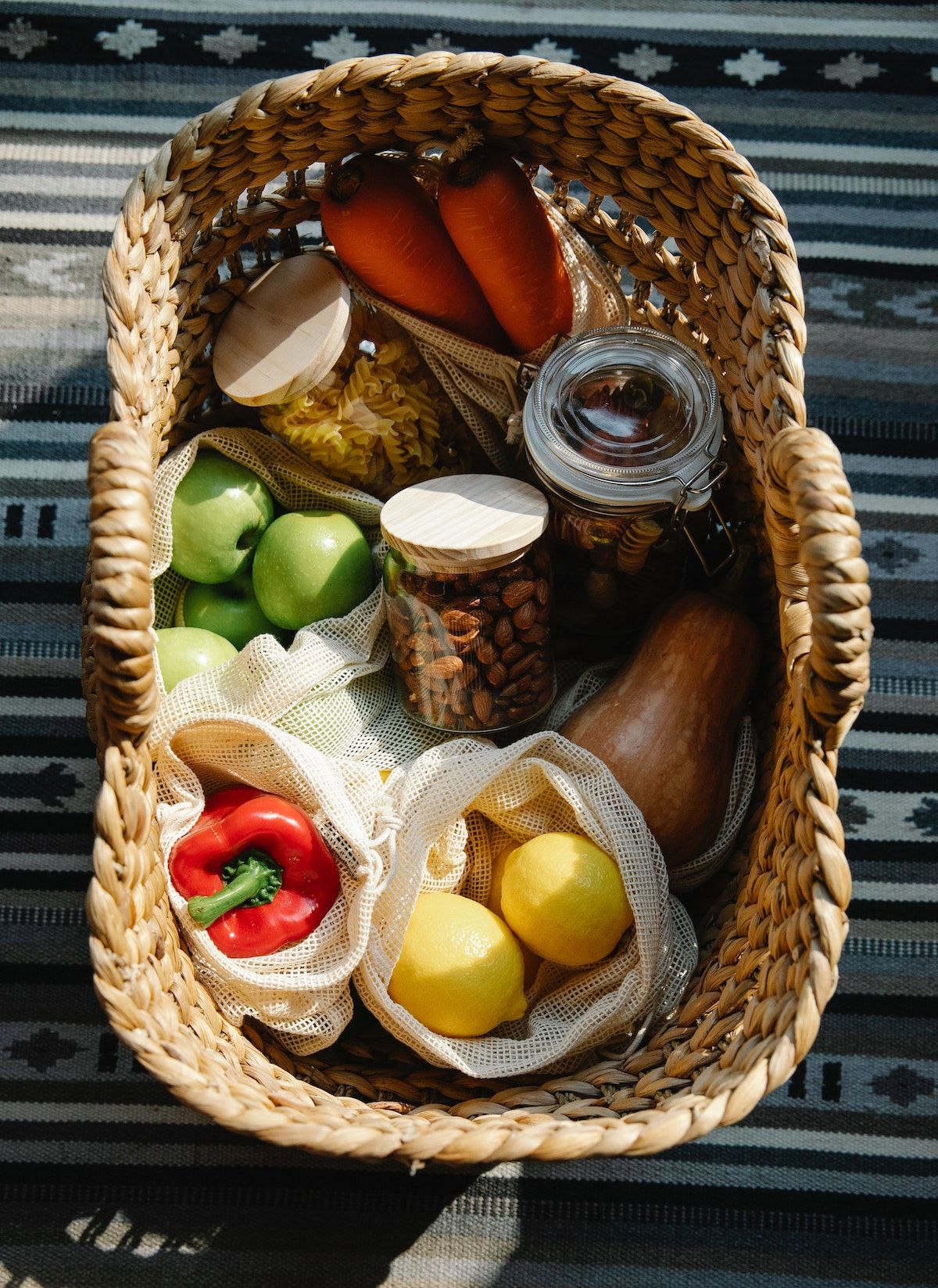 Ein Picknick-Korb mit Nudeln, Nüssen, Obst und Gemüse liegt auf einer Decke.